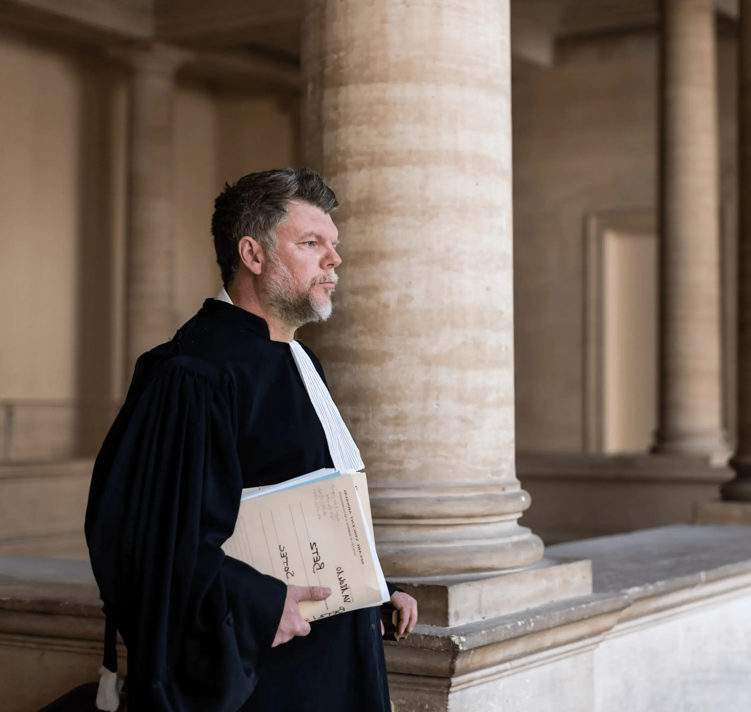 Maître Vincent Arnaud en robe d'avocat, un dossier sous le bras, sous les colonnes du palais de justice
